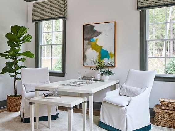 Bright white chairs around a square table in a living room with black-trimmed windows