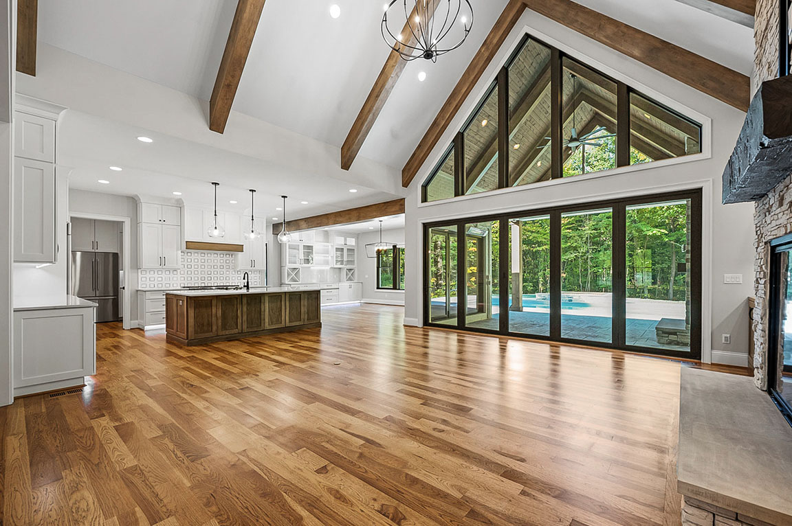 Spacious open floor plan with vaulted ceiling, wood beams, large windows, and hardwood floors.