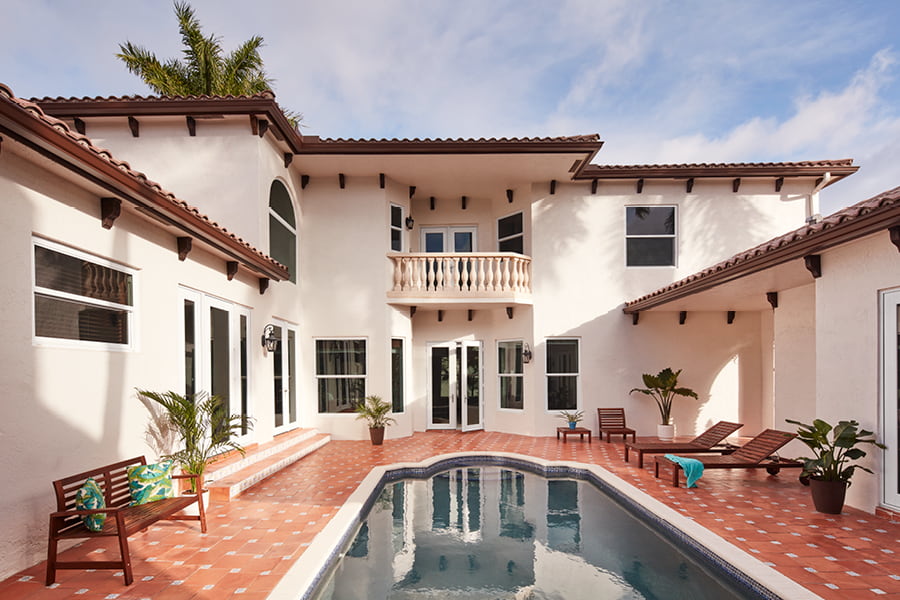 Exterior white home with Hurricane Shield windows, red tiled outdoor space and pool
