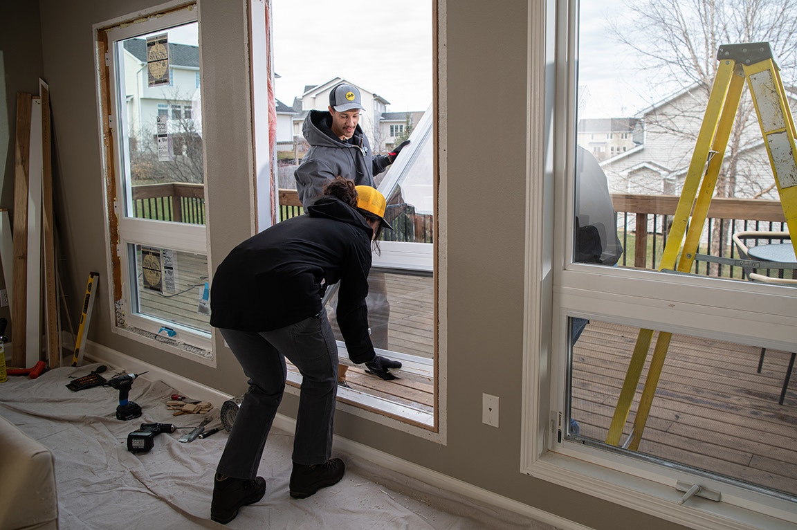 A modern bathroom with two black windows, white walls, and a wooden stool, featuring a stylish sink.