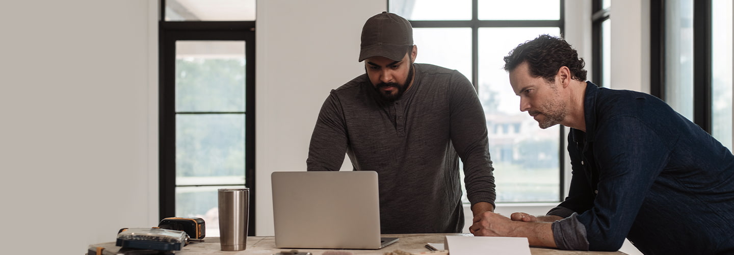 two men looking at a laptop in a home under construction