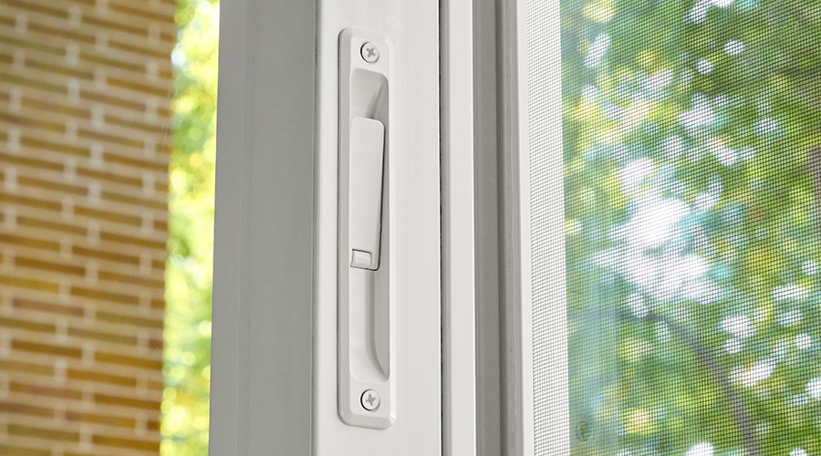 Close-up of a white sliding door handle with trees visible through the screen.