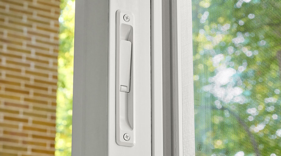 Close-up of a white sliding door handle with trees visible through the screen.