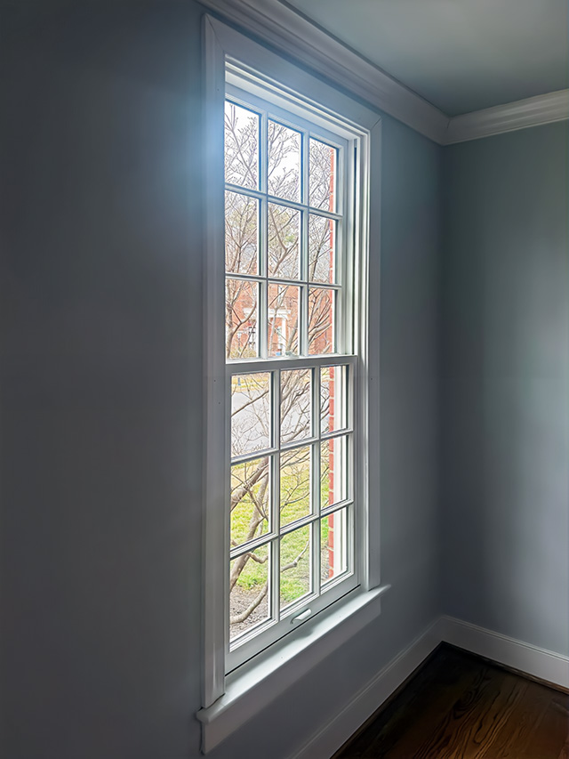 Interior view of a white double‑hung window with traditional grilles and natural light in a classic home.