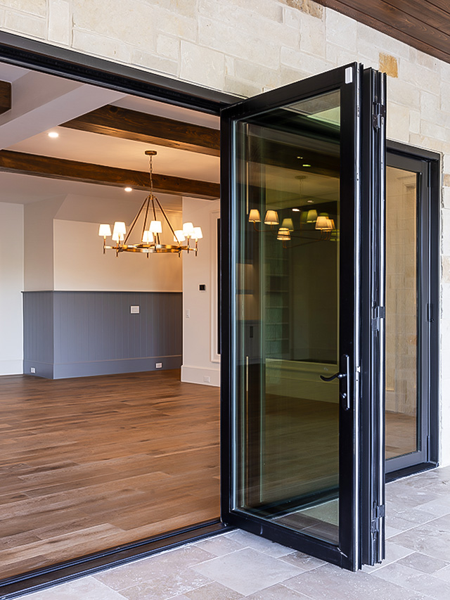 An elegant dining area highlighted by folding glass doors, wooden floors, and a chandelier hanging from the ceiling.