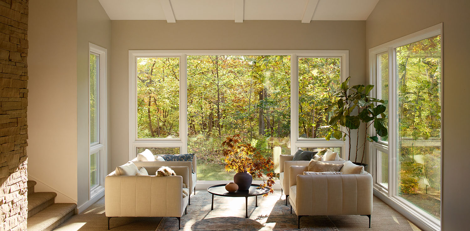 Replacement of large windows in a modern living room with beige sofas and a view of trees.