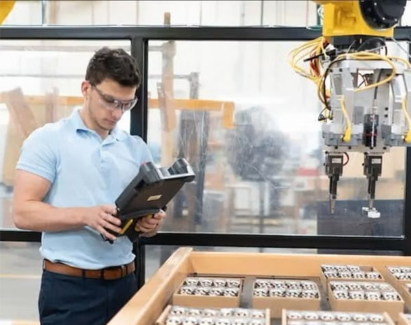 A Pella manufacturing team member is adjusting a custom robotic device.