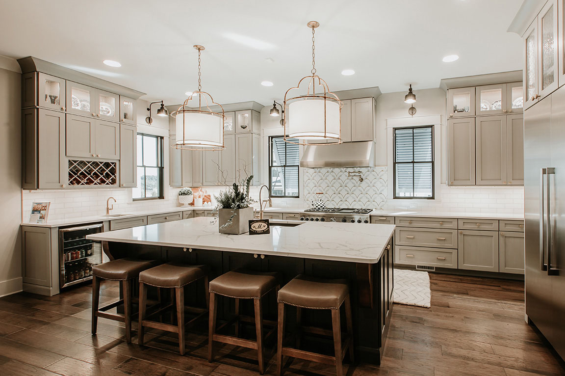 A modern kitchen with a large island, and kitchen windows, featuring pendant lights and stainless steel appliances.