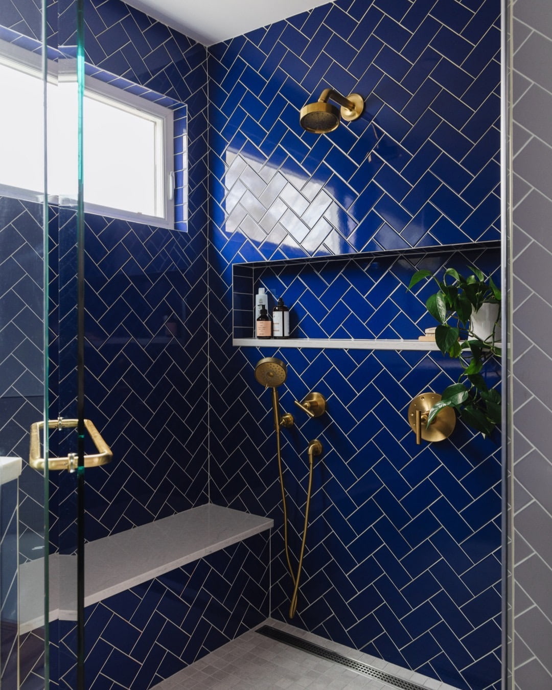 A shower with royal blue tile has a white shower window placed high on one wall.