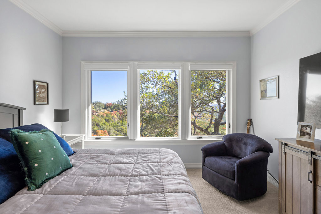 Bright bedroom with three large windows offering outdoor tree and hillside views.
