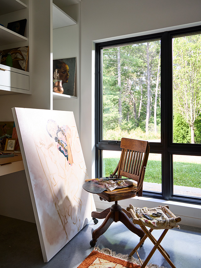 An artist's chair beside a large painting in a bright room with black windows, showcasing a black window art room.