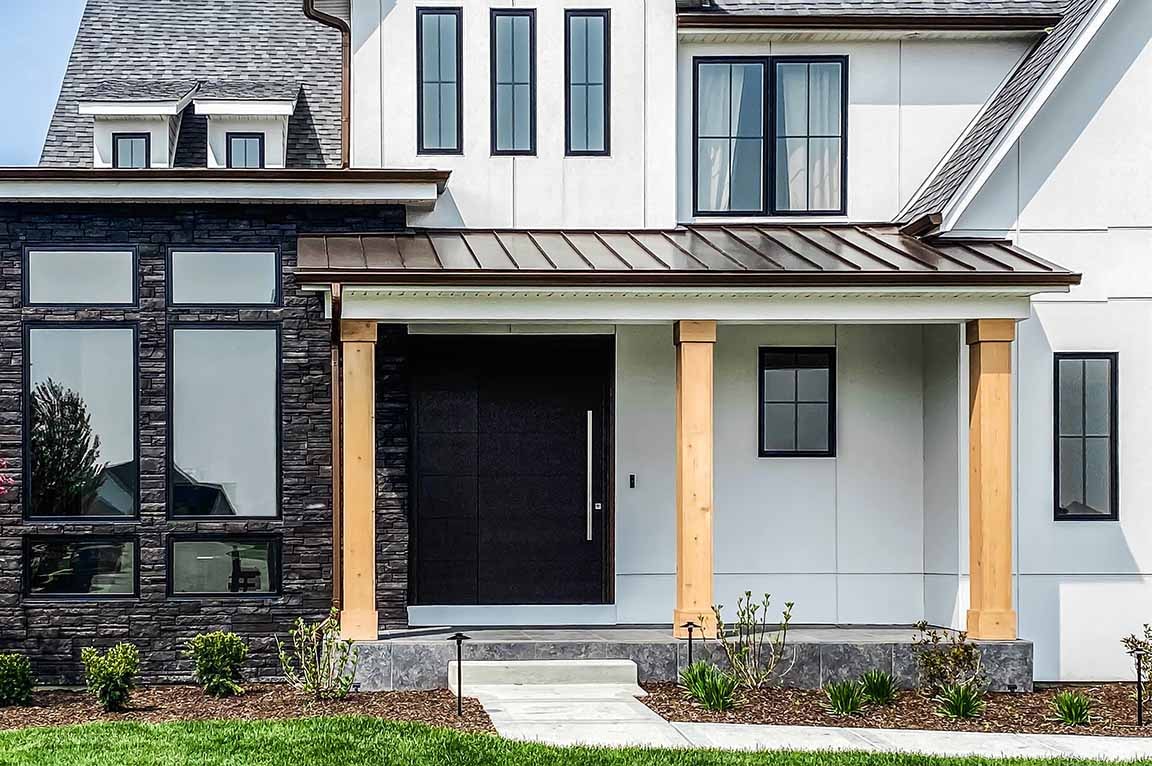 Modern farmhouse front entry with black windows, wood columns, and stone accents.