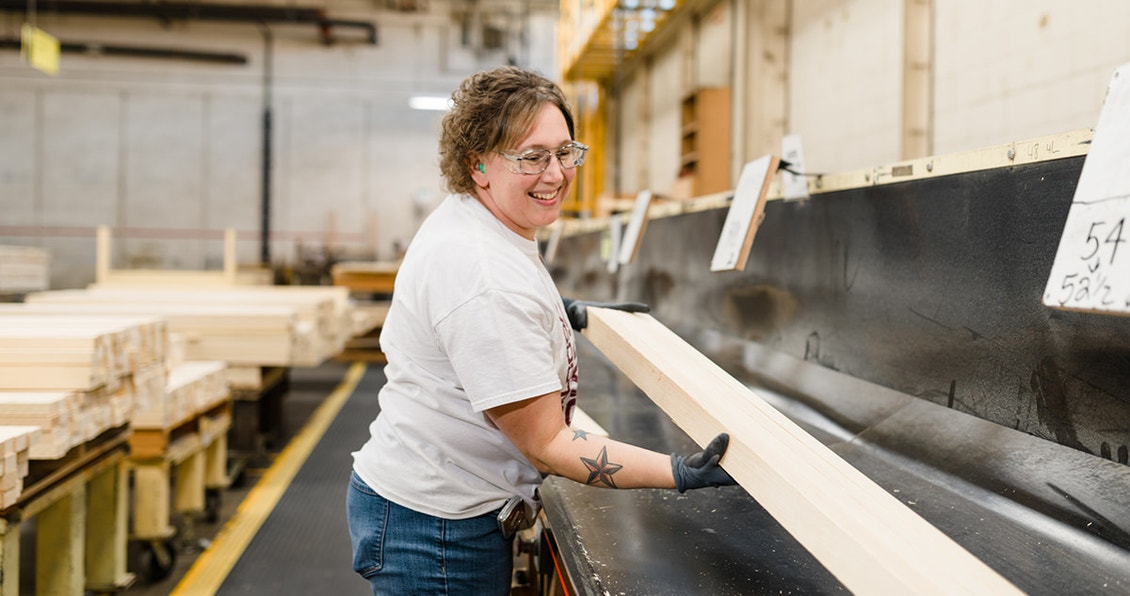 female factory working with a long sheet of wood to be used in windows