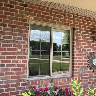 An almond-colored sliding window on a brick home is outdated.