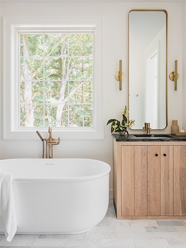 a white soaker tub aside a vanity with a tall narrow mirror