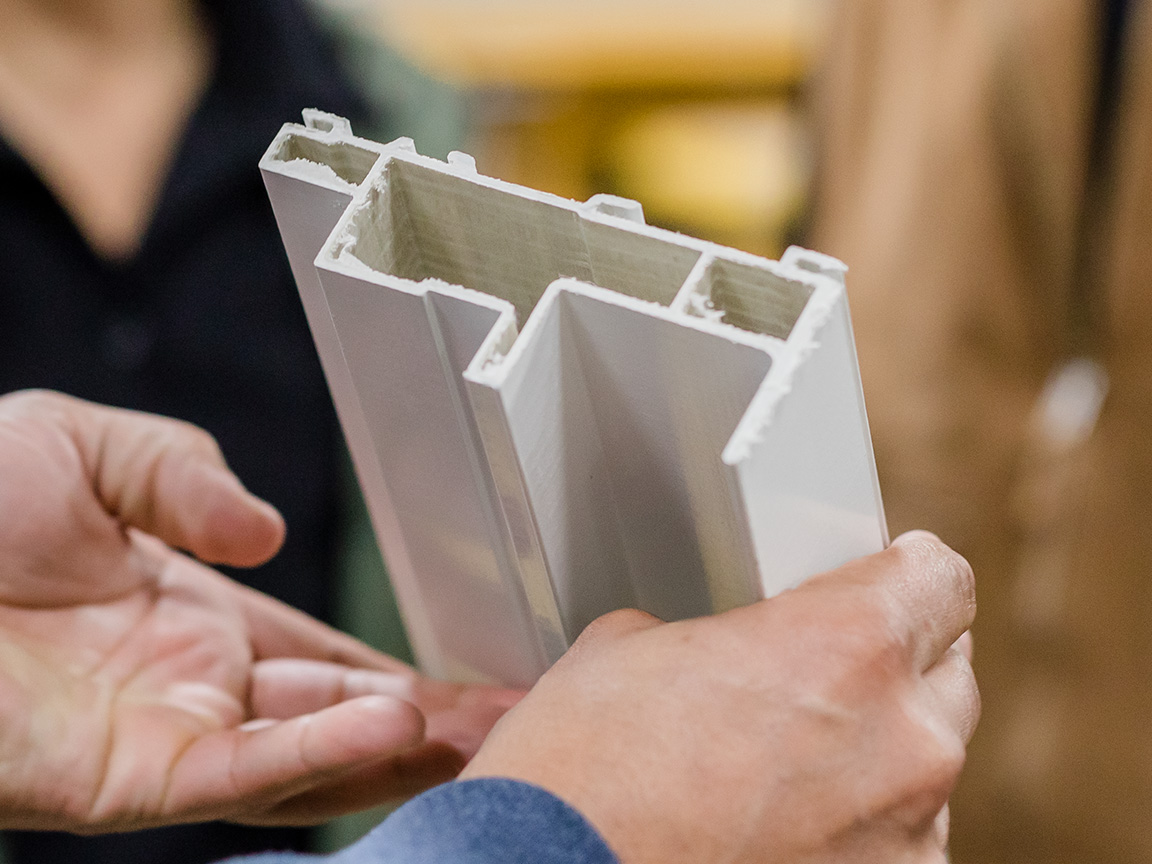 Hands holding a window frame cross-section showing internal structure and materials.