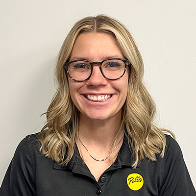 A smiling team member with glasses and tattoos stands in front of a large wall logo.