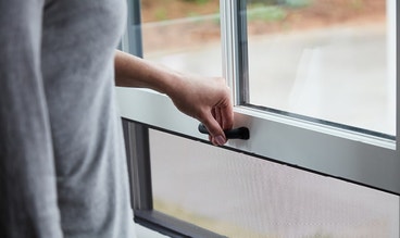 woman lifting a double-hung window exposing a screen