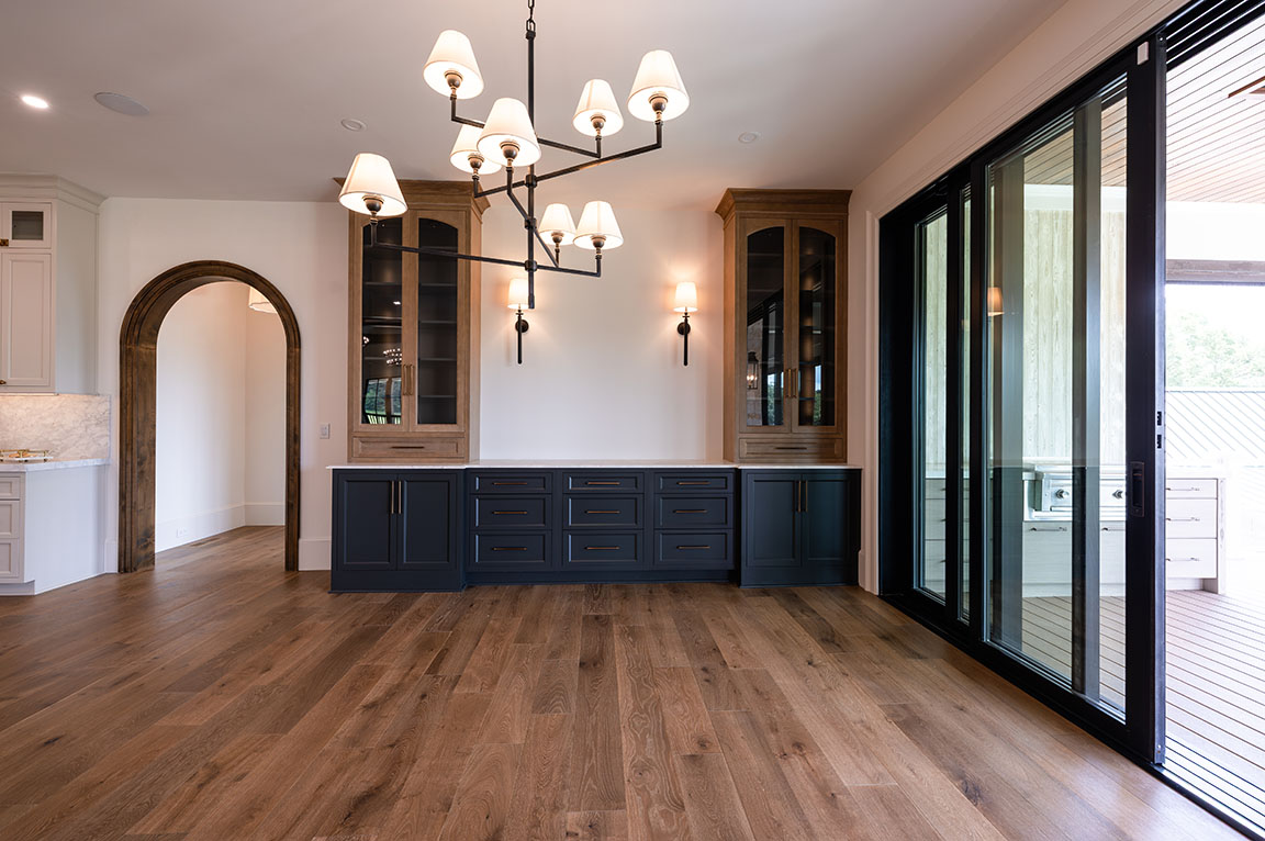 Spacious modern dining room featuring hardwood floors, a large chandelier, built-in cabinetry with glass doors, and sliding glass doors leading to an outdoor area.