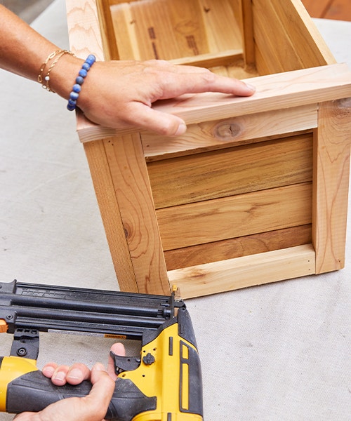 Using a nail gun to attach a cedar board to a wood window box.
