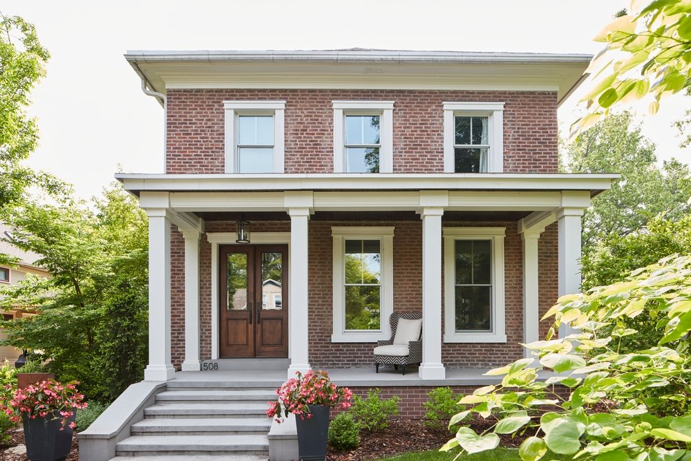 Two story red brick house with white double-hung windows and a wood double door with glass