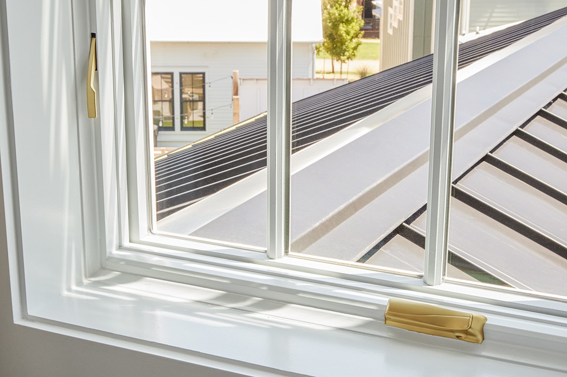 A close-up view of window glass in a white frame with a golden handle, showcasing a modern home setting.