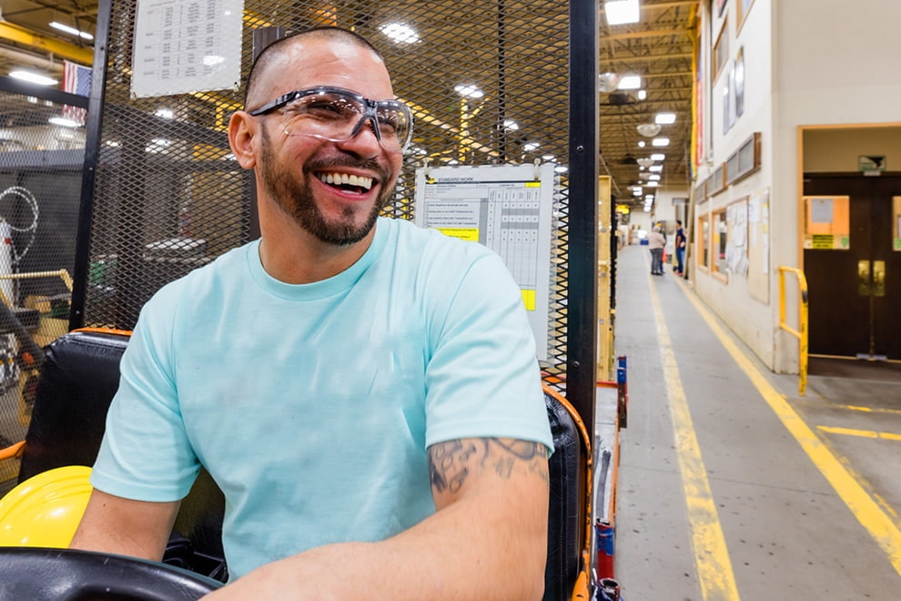 a manufacturing worker driving a forklift while smiling and enjoying his job