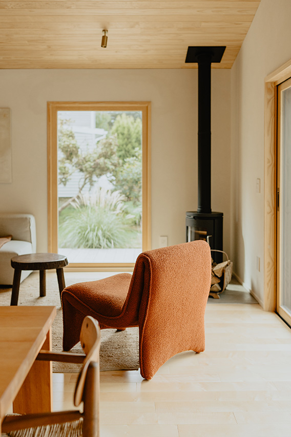 A modern living room with energy efficient windows, a wood stove, and a rust-colored chair facing a large glass door.