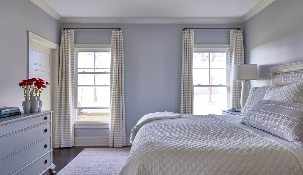 Neutral colored bedroom with bed in front of two double-hung vinyl windows with white & gray striped curtains