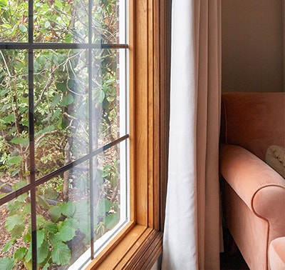 the right side of a new Pella wood window with a pink chair next to the drapery
