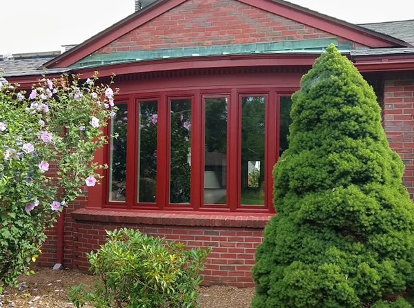 A red bow window protrudes with a gentle curve from the exterior of a brick home. 