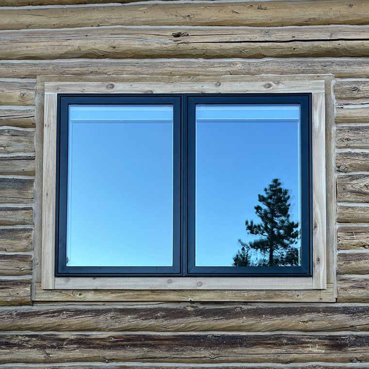 Black windows in a wooden cabin, reflecting the sky and trees, illustrating an after window.