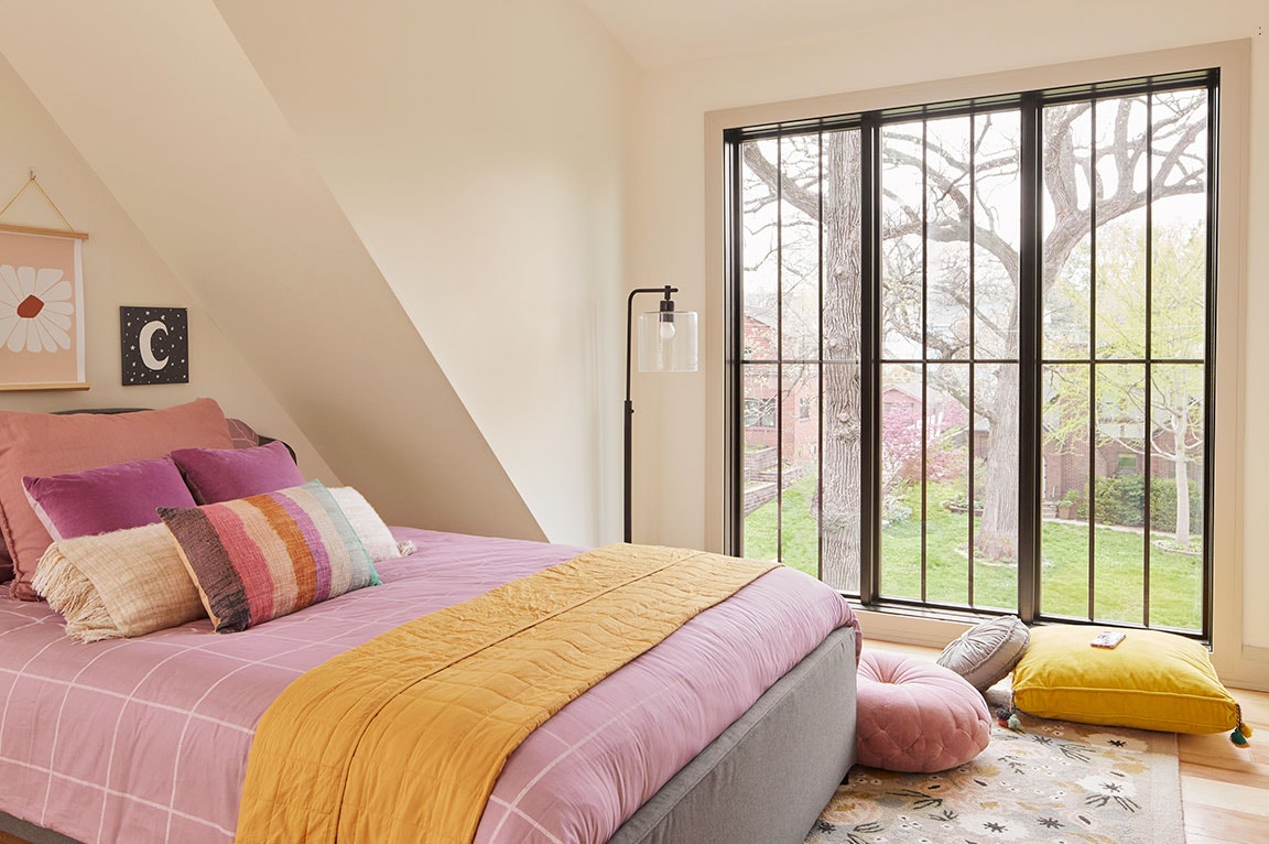 A pink bedroom with floor-to-ceiling windows, colorful pillows, and a cozy, modern decor.