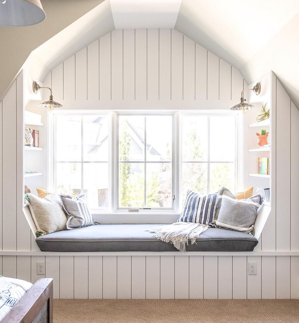 A bedroom window seat adorned with decorative pillows lies below white casement windows.