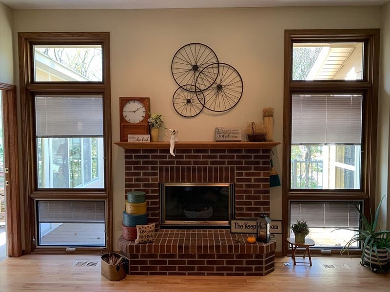 Two window units, each consisting of a casement with awning below, sit on each side of a traditional brick fireplace.