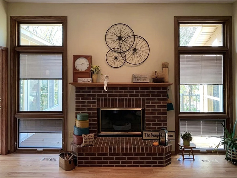 Two window units, each consisting of a casement with awning below, sit on each side of a traditional brick fireplace.