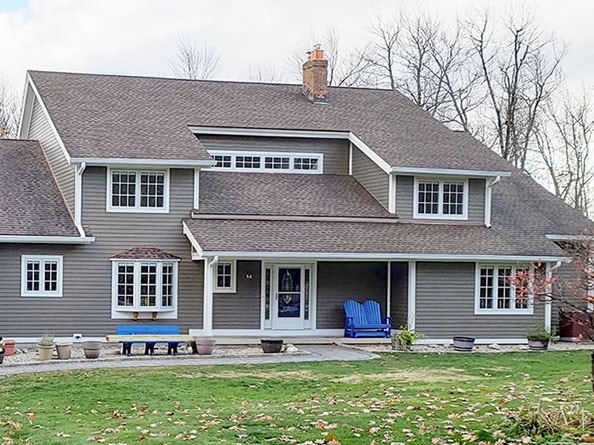 West Granby modern house with gray siding and white windows, featuring a porch and blue chairs in the front yard.
