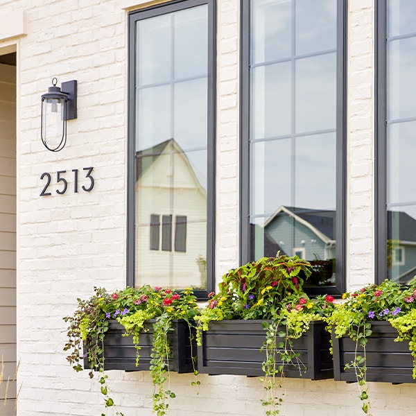 black window boxes sit under casement windows on a white brick home exterior