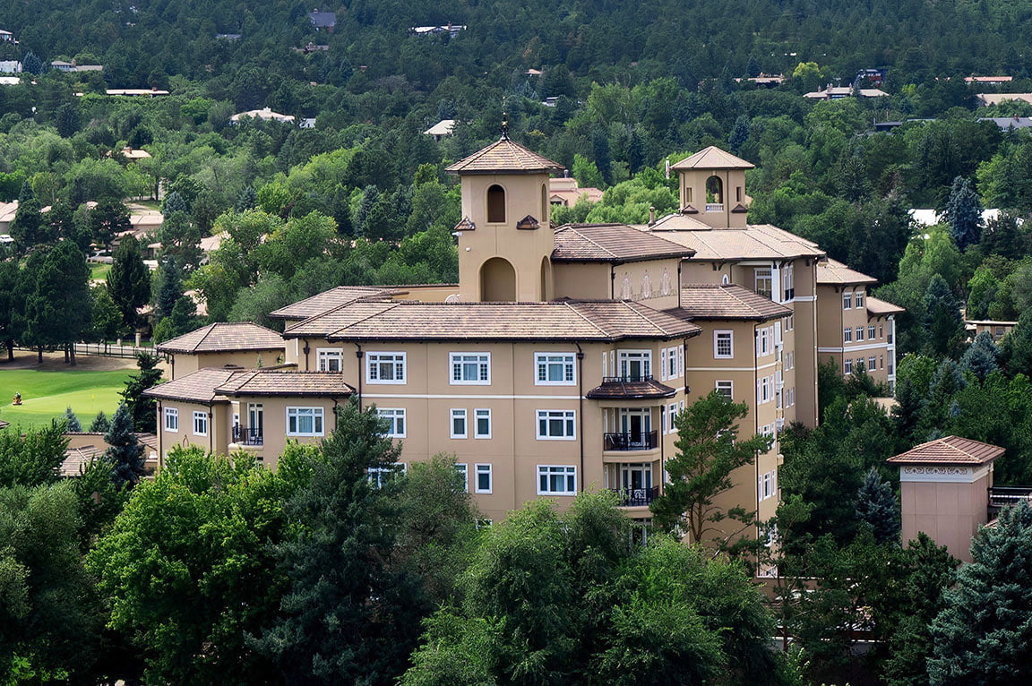 A modern building surrounded by lush trees, featuring multiple casement windows.