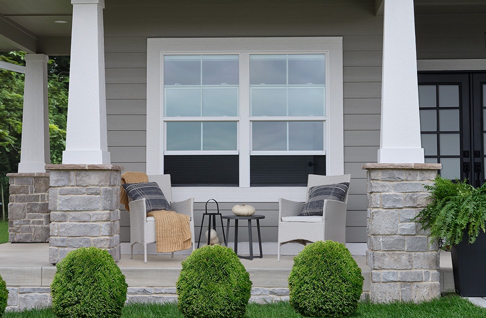 two white single-hung windows that connect a traditional front porch with the gray home interior