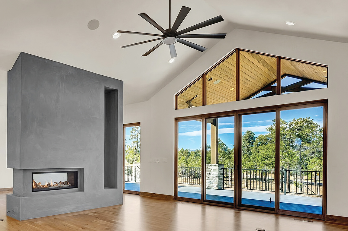 A large living room with a custom fireplace, wood floors, and a wood four-panel sliding patio door, all overlooking the mountains outside.