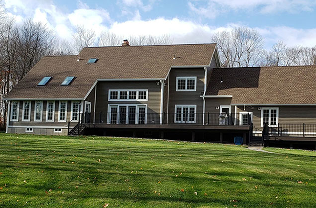 A modern home exterior featuring wood windows with a bench and chairs on the porch.