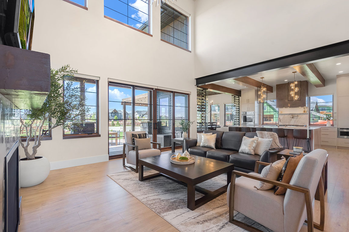 Spacious open-concept living room with neutral-toned furniture, large windows, hardwood floors, and view into a contemporary kitchen with marble island and pendant lights.