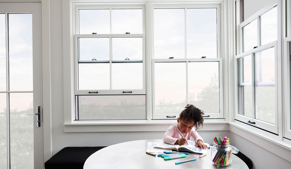 girl coloring at table with white double-hung windows with integrated screen behind her