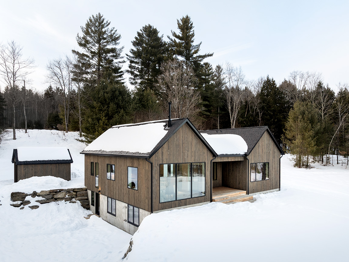 A modern house in a snowy landscape featuring large fiberglass windows and wooden siding.