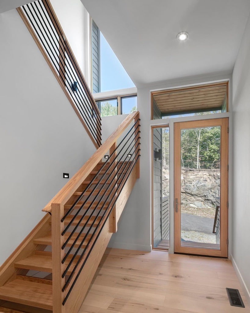 A modern entryway features a wood front door with full glass and a wood staircase with picture windows.