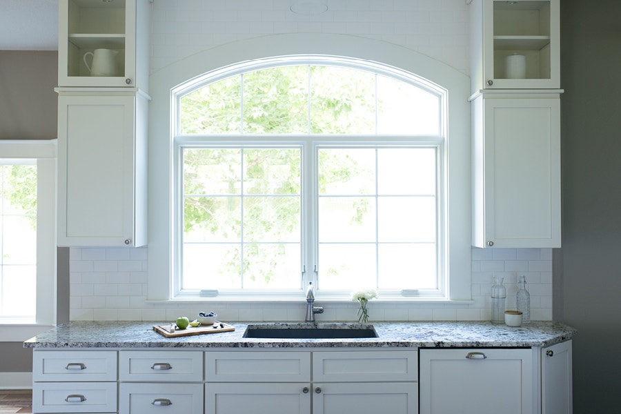 White trim arched transom set over two casement windows above the kitchen sink