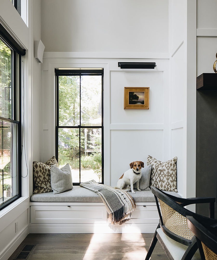 A dog sits on the window seat below black double-hung windows in a contemporary dining room.