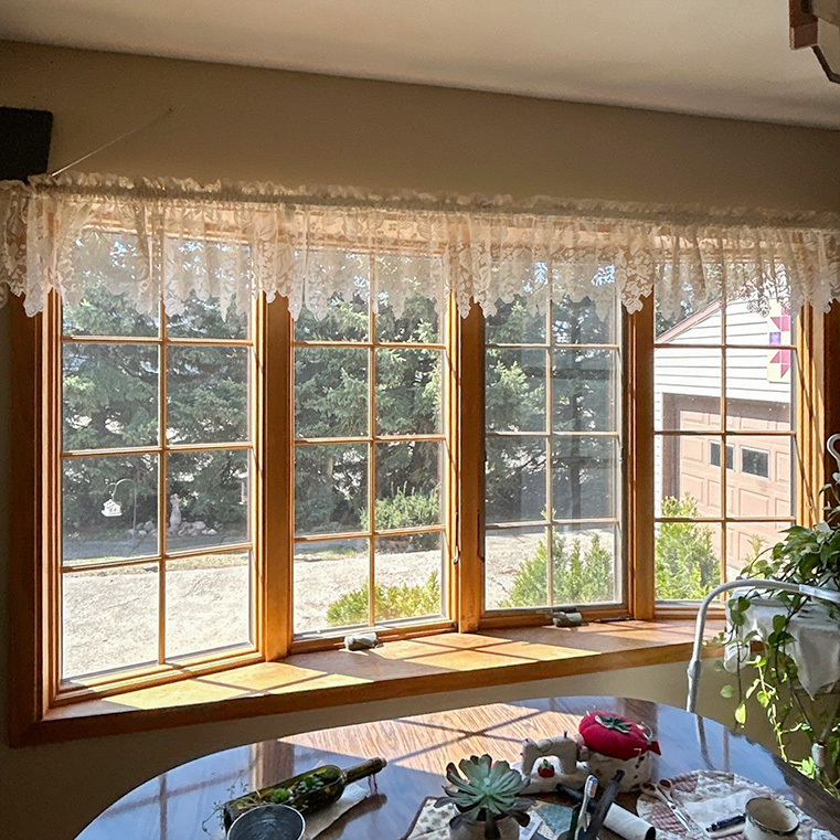 Interior view of a bow window with lace curtains overlooking a garden.