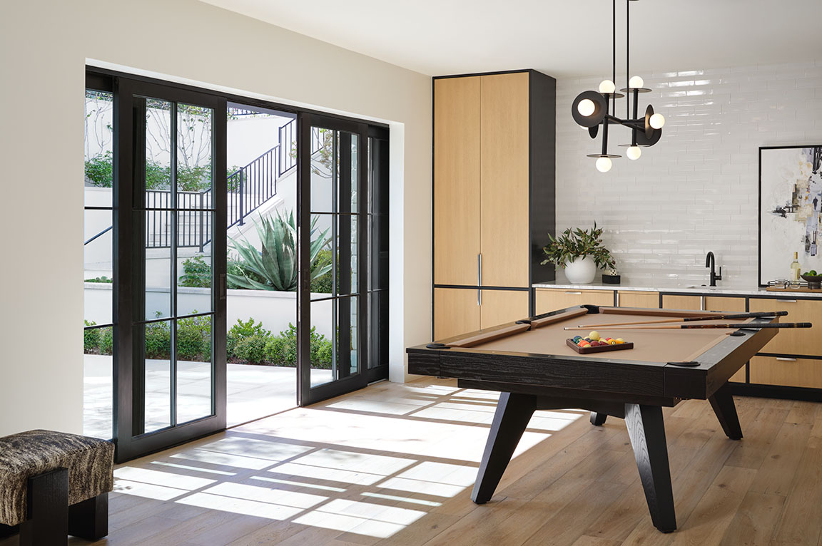 A rec room opens to the outdoors via a large black multi-slide patio door.